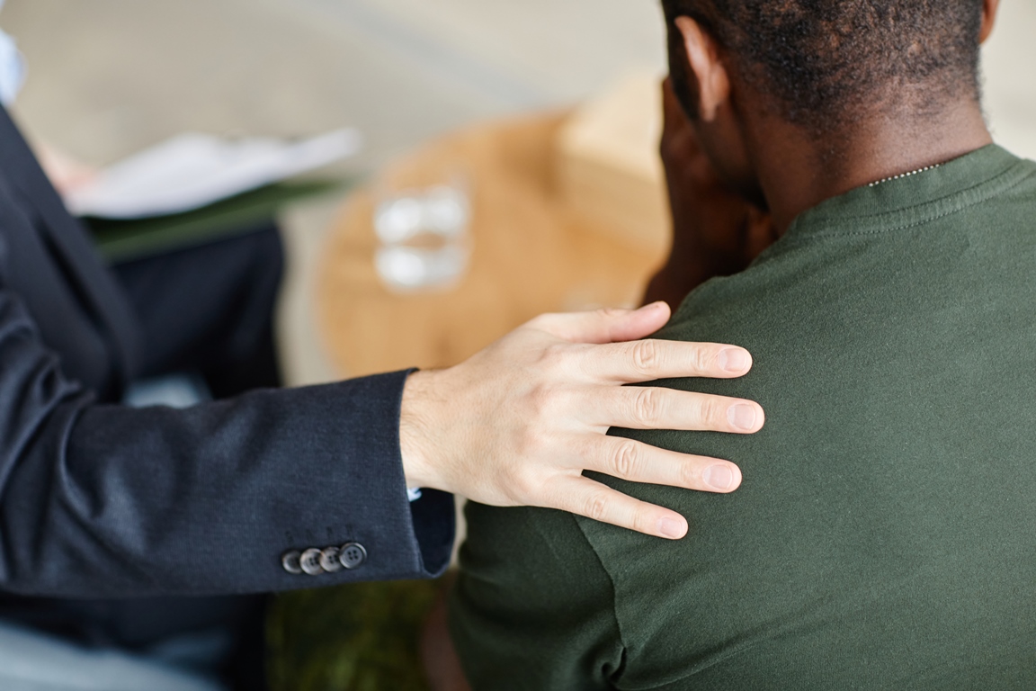 Unrecognizable professional psychologist comforting Black soldier suffering depression touching his shoulder